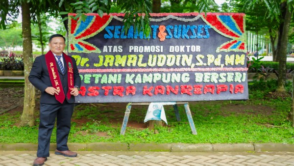 Dr Jamaluddin, S.Pd, MM, petani milenial asal Kanreapia, Gowa, berpose di depan papan ucapan selamat usai dinyatakan lulus ujian promosi doktor di UIN Alauddin Makassar.